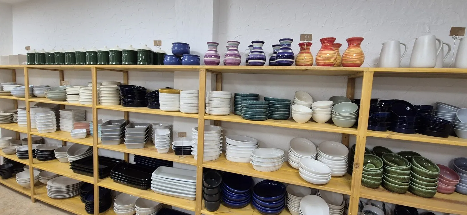 Estanterías de madera de la tienda llenas de jarras, cuencos y platos de colores